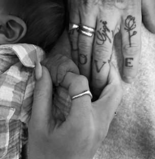 Black and white photo of a newborn's hand grasping an adult's hand.