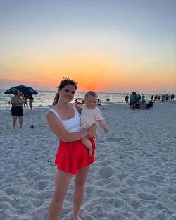 Woman holding baby on beach at sunset.