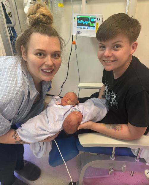 Two women holding their newborn twins in a hospital.