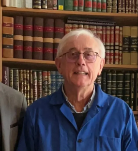 Man in blue jacket in front of bookshelves.