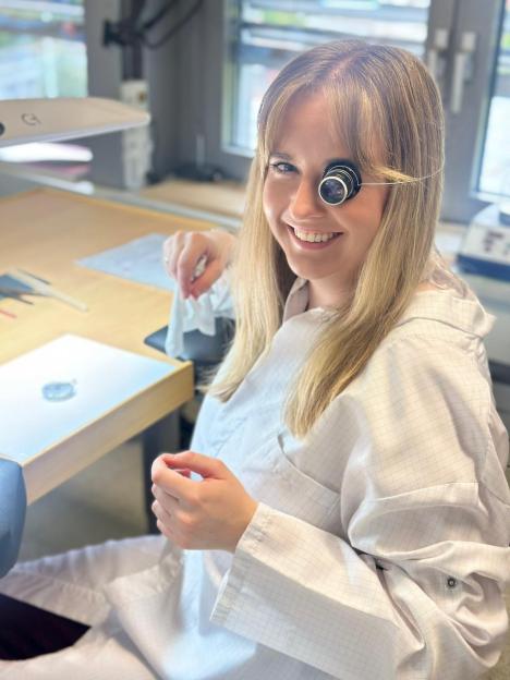 Smiling female watchmaker wearing a loupe.