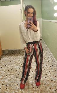 Woman in striped pants taking a selfie in a bathroom.