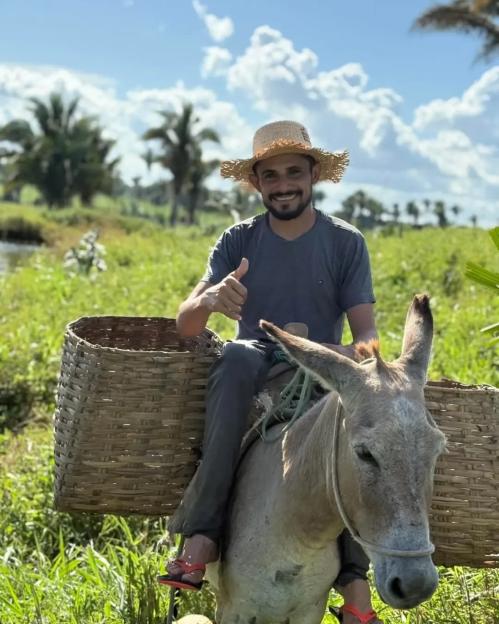 Reinaldo da Silva Melo, also known as the "King of Juquira" influencer, riding a donkey in a field and giving a thumbs up.