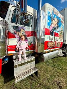 Toddler standing on step of a semi-truck decorated with Mickey and Minnie Mouse.
