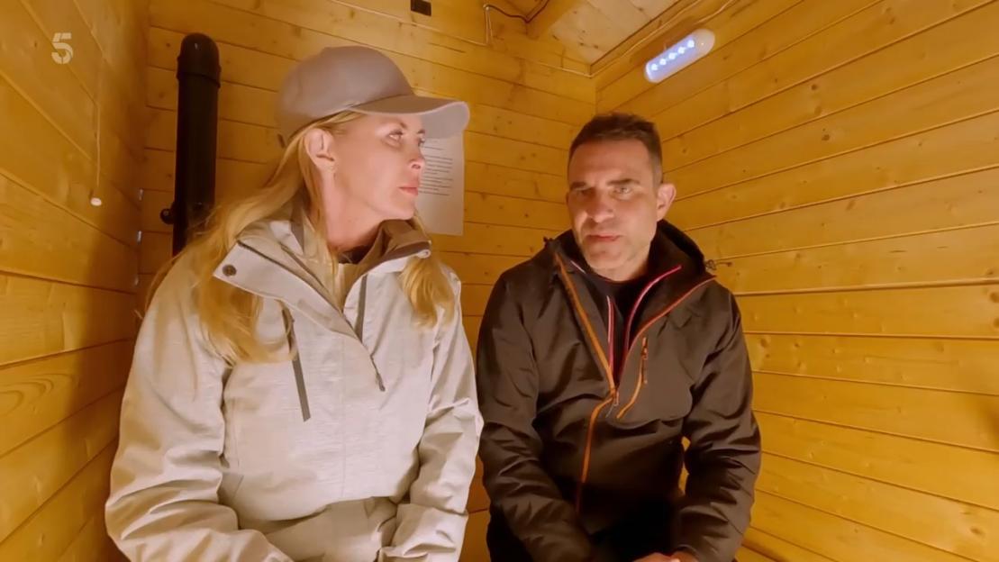 Screenshot from Rich Holiday Poor Holiday showing a man and woman sitting in a small wooden room.