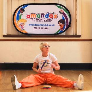 Woman in orange pants playing percussion instruments in front of Amanda's Action Club banner.