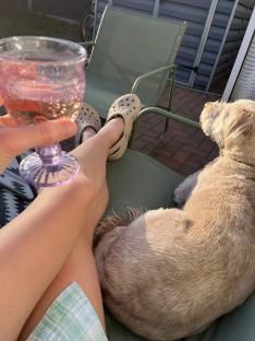 Person's legs resting on a chair with a dog and a glass of rosé.