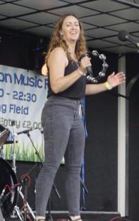 Woman singing on stage with tambourine.