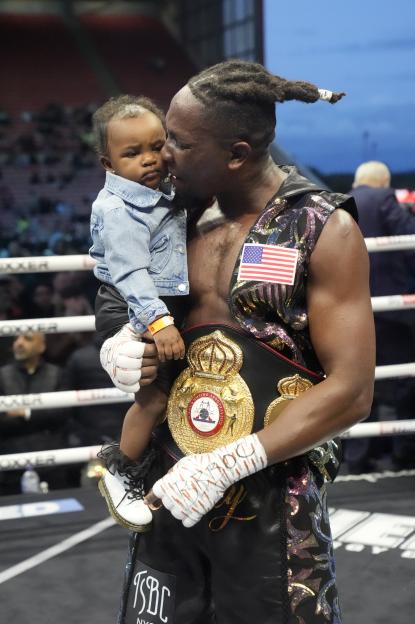 A boxer holds his child and championship belt after a win.