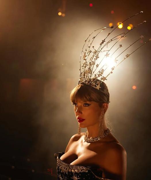 Taylor Swift in a bejeweled headdress with star-shaped accents and a low-cut dress, with bright light behind her.