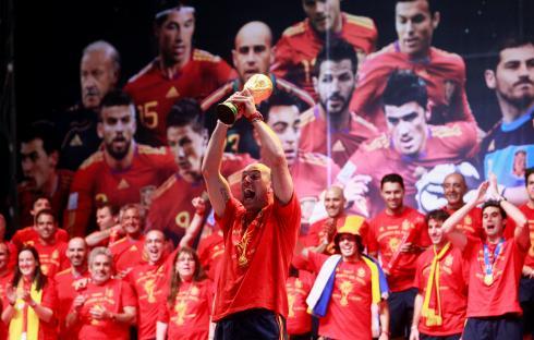 A man in a red shirt lifts the World Cup trophy, surrounded by a crowd of people also wearing red.