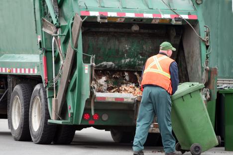 Sanitation worker emptying a green bin into a garbage truck.