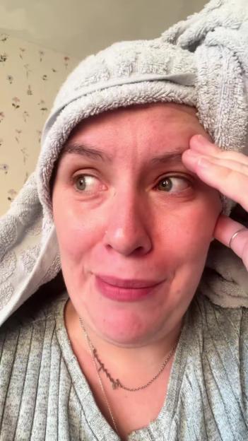 A woman with a towel wrapped around her head has an embarrassed expression, looking to the side with her hand on her forehead.