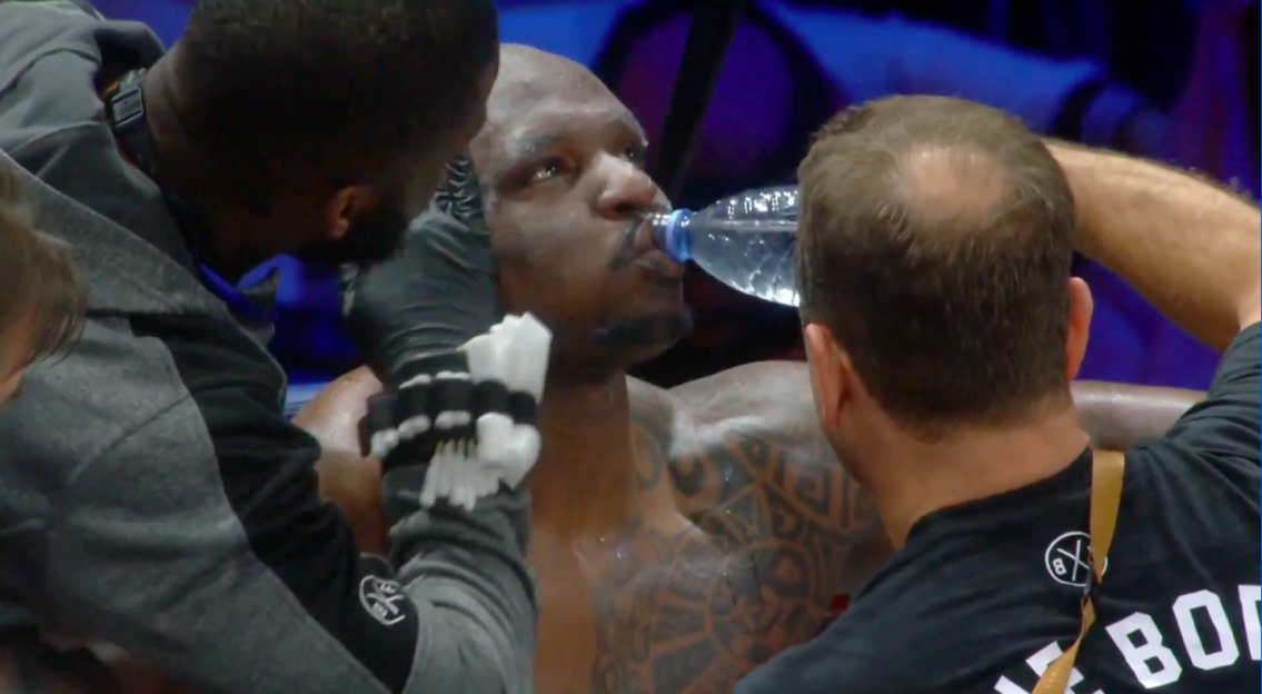 Screenshot of a boxer drinking water while his cornerman cleans his face.