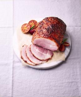 Honey-glazed ham slices on a marble platter with orange slices and plums.