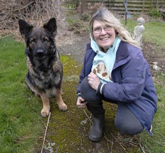 Woman squatting with her German Shepherd dog in a garden.