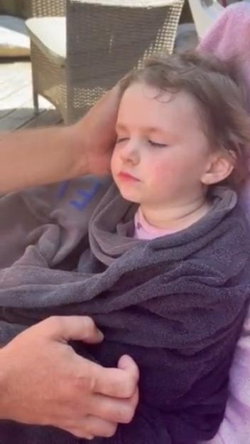 A young girl, Teraysa, wrapped in a blanket with her eyes closed, as an adult's hands gently rest on her head and shoulder.