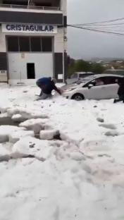 Person clearing hail from car after hailstorm.