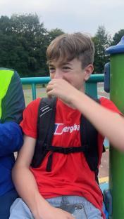 Teenage boy laughing, wearing a red shirt and backpack.