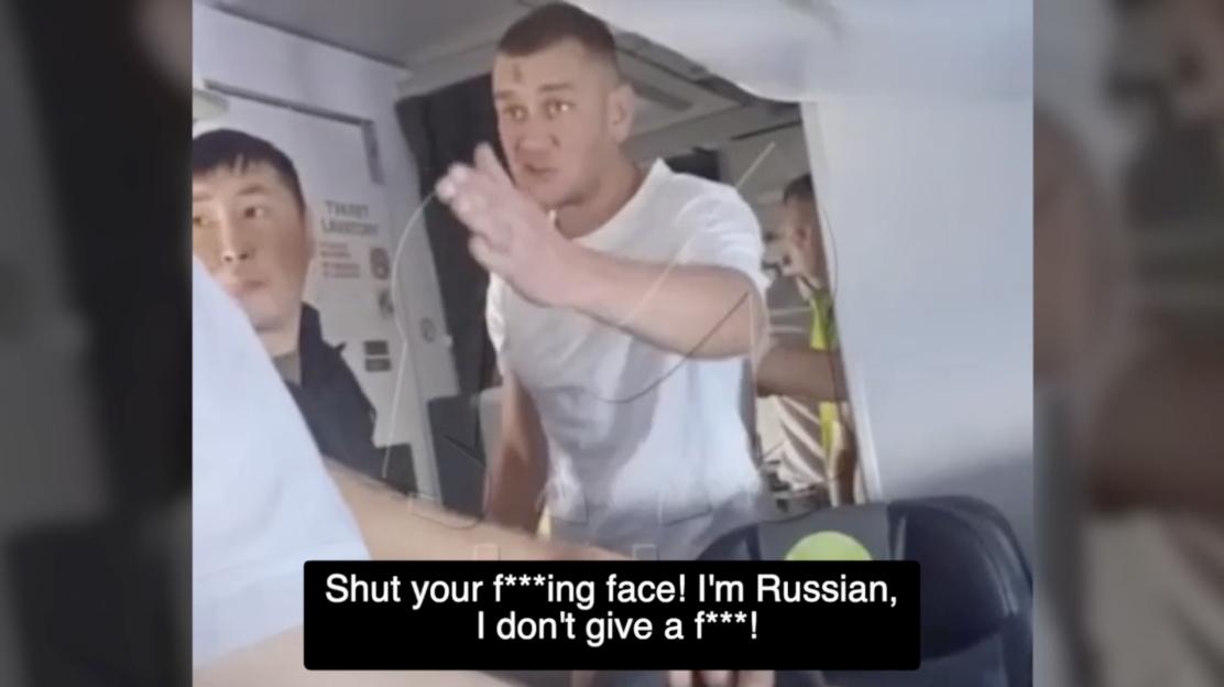 A man on an airplane yelling at another passenger.