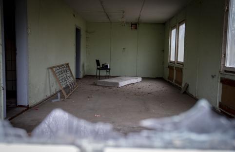 Interior of dilapidated room with mattress, chair, and bed frame.