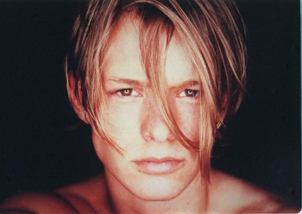a young man with long blonde hair looks at the camera