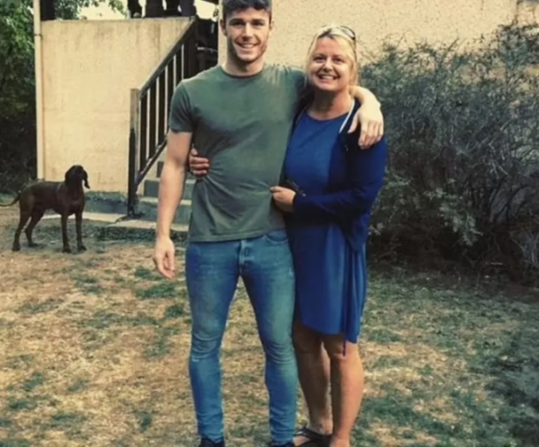 Man and woman embracing outdoors with a dog in the background.