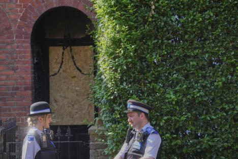 Two police officers standing outside a house with a boarded-up door.