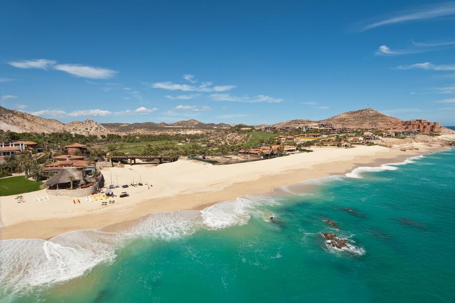 Aerial view of a beach in Cabo San Lucas, Mexico, with turquoise water, sand, and buildings by the shore.