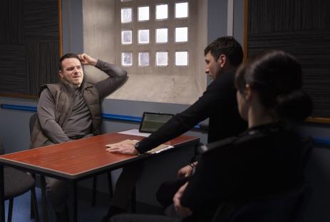 A suspect sits across from two interviewers during a police interview.