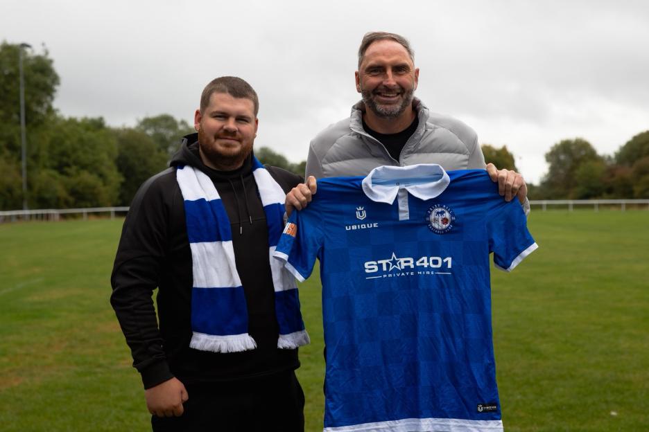 Two men on a soccer field holding up a Daisy Hill Football Club jersey.