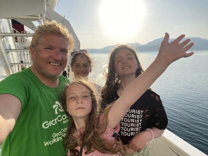 Family selfie on a ferry, overlooking the sea and mountains.