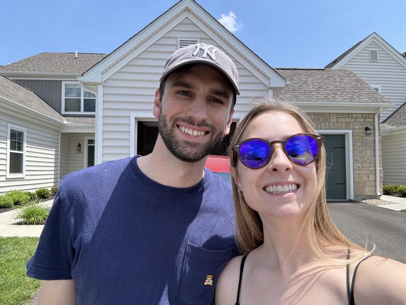 A couple smiles for a selfie in front of their new home.