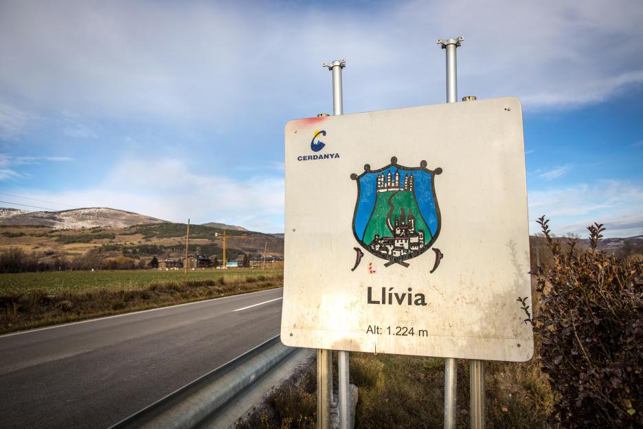 Welcome sign for Llívia, Spain with a blue sky and mountains in the background.