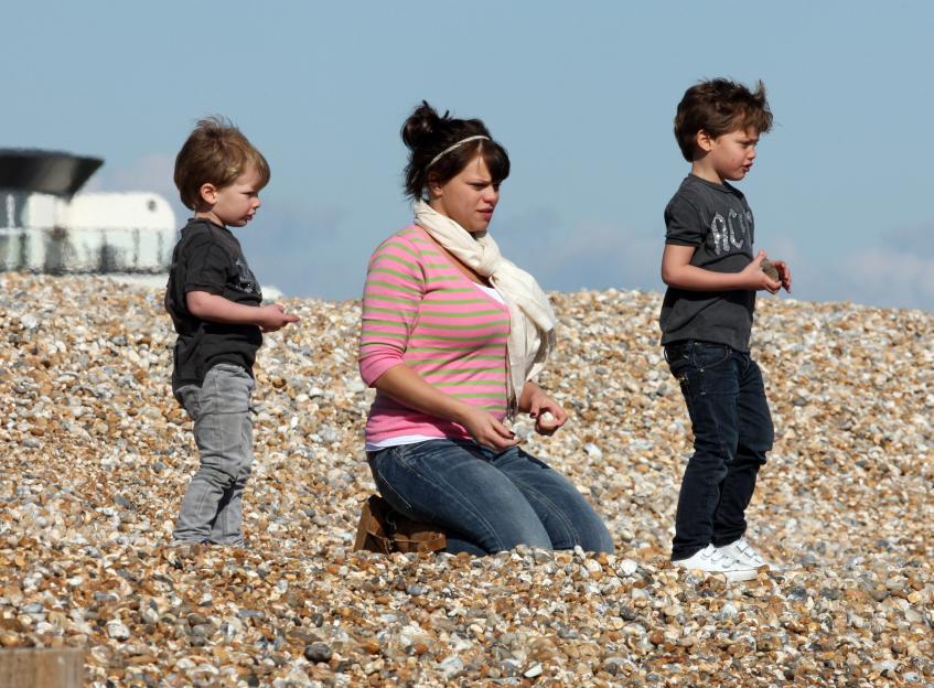 A woman and her two young sons playing on a pebble beach.