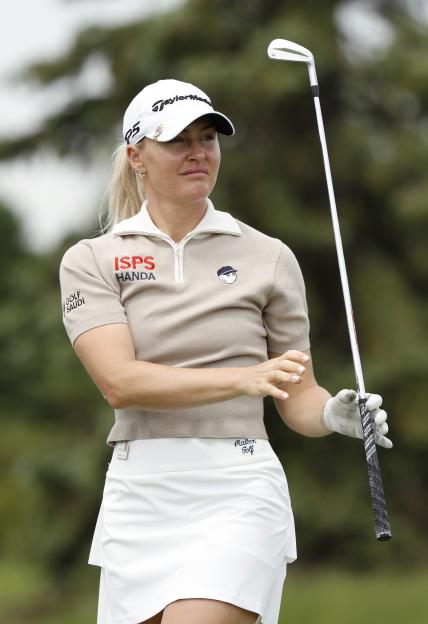 Charley Hull holding a golf club, wearing a white cap, light brown top, and white skirt.