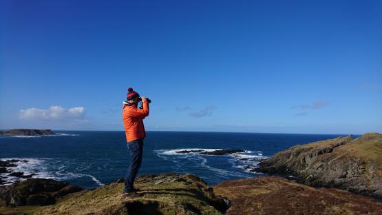 Person using binoculars overlooking the ocean from a cliff.