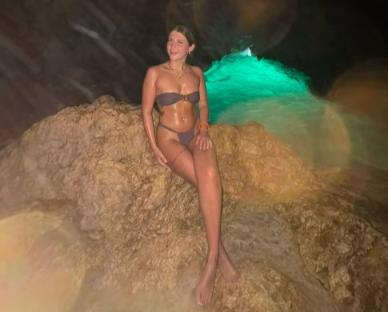 Woman in bikini sitting on rocks near water.