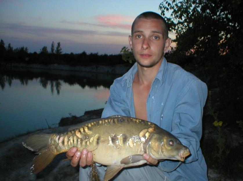 Man holding a large fish by a lake at sunset.