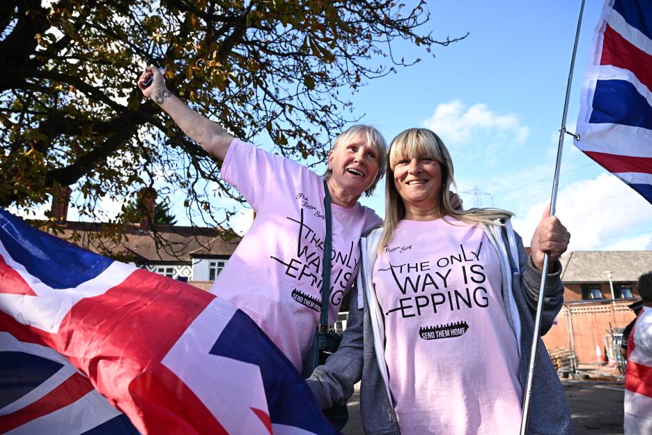 Protesters in Epping, England, holding Union Jack flags and wearing shirts that read "The only way is Epping. Send them home."
