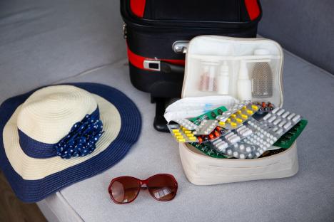 Beach hat, sunglasses, and a first-aid kit with medication next to a suitcase.