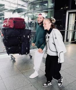 Jojo Siwa and Chris Hughes holding hands at an airport, luggage in tow.
