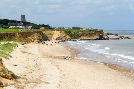 Happisburgh Beach in North Norfolk, England, with people on the sandy beach and a church visible in the distance.