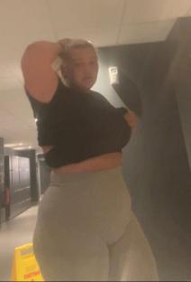 Woman in a gym hallway changing her shirt.
