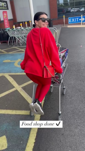Woman in red riding a shopping cart in a supermarket parking lot.