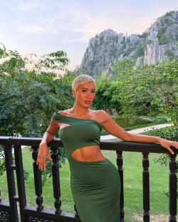 Woman in green dress on balcony overlooking mountains.