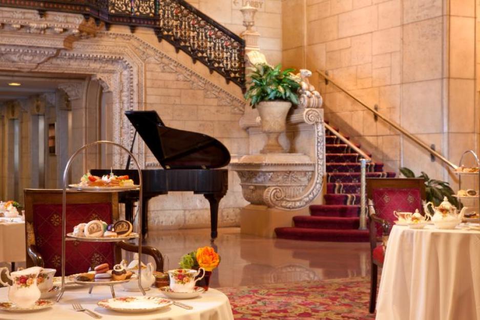 Afternoon tea setting with pastries and teacups in a hotel lobby with a grand piano and staircase.