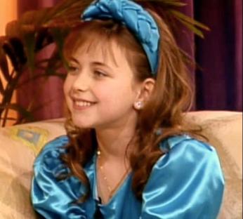 a young girl wearing a blue satin dress and a blue headband is sitting on a couch .