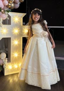 Girl in white dress standing next to a lighted cross and balloon arch.