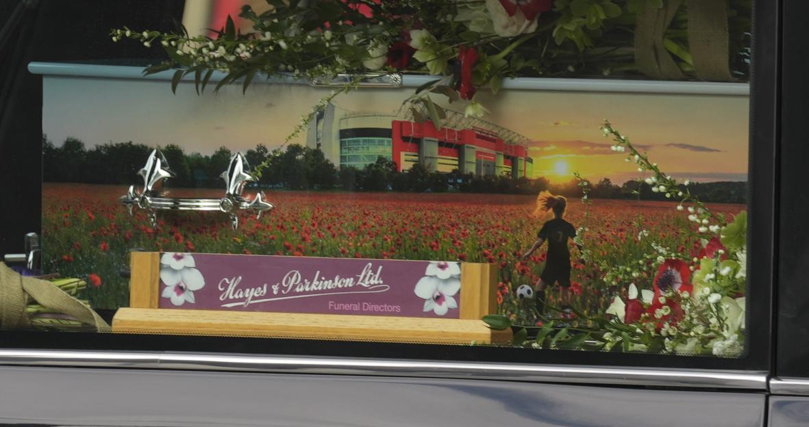 Image of a hearse with a coffin decorated with a picture of a poppy field, a stadium, and a child playing soccer.